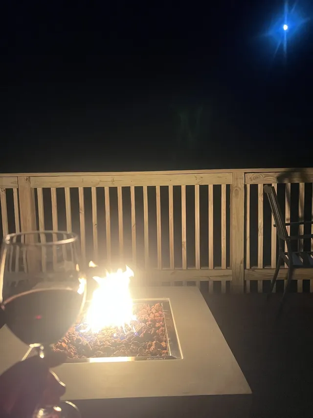 A fire pit burns on a deck beneath a dark night sky.