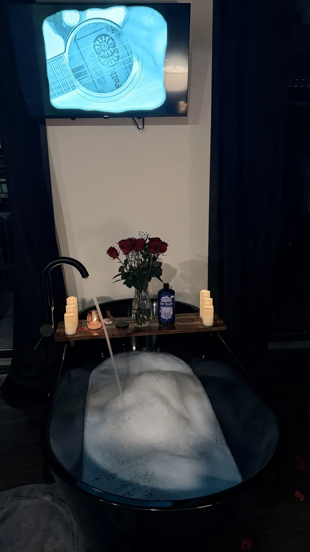 A freestanding tub filled with bubbles sits beneath a wall-mounted television.