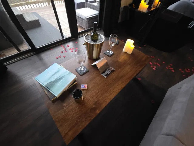 Wine, glasses, candles, and rose petals are arranged on a wooden table.