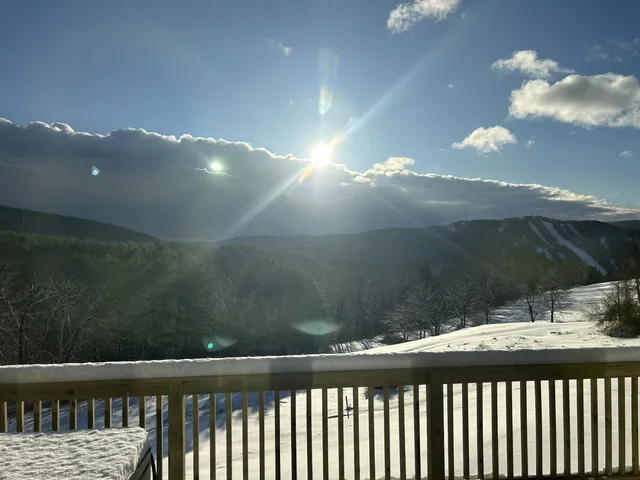 Sunlight breaks through clouds over snowy mountain slopes and a cabin deck.