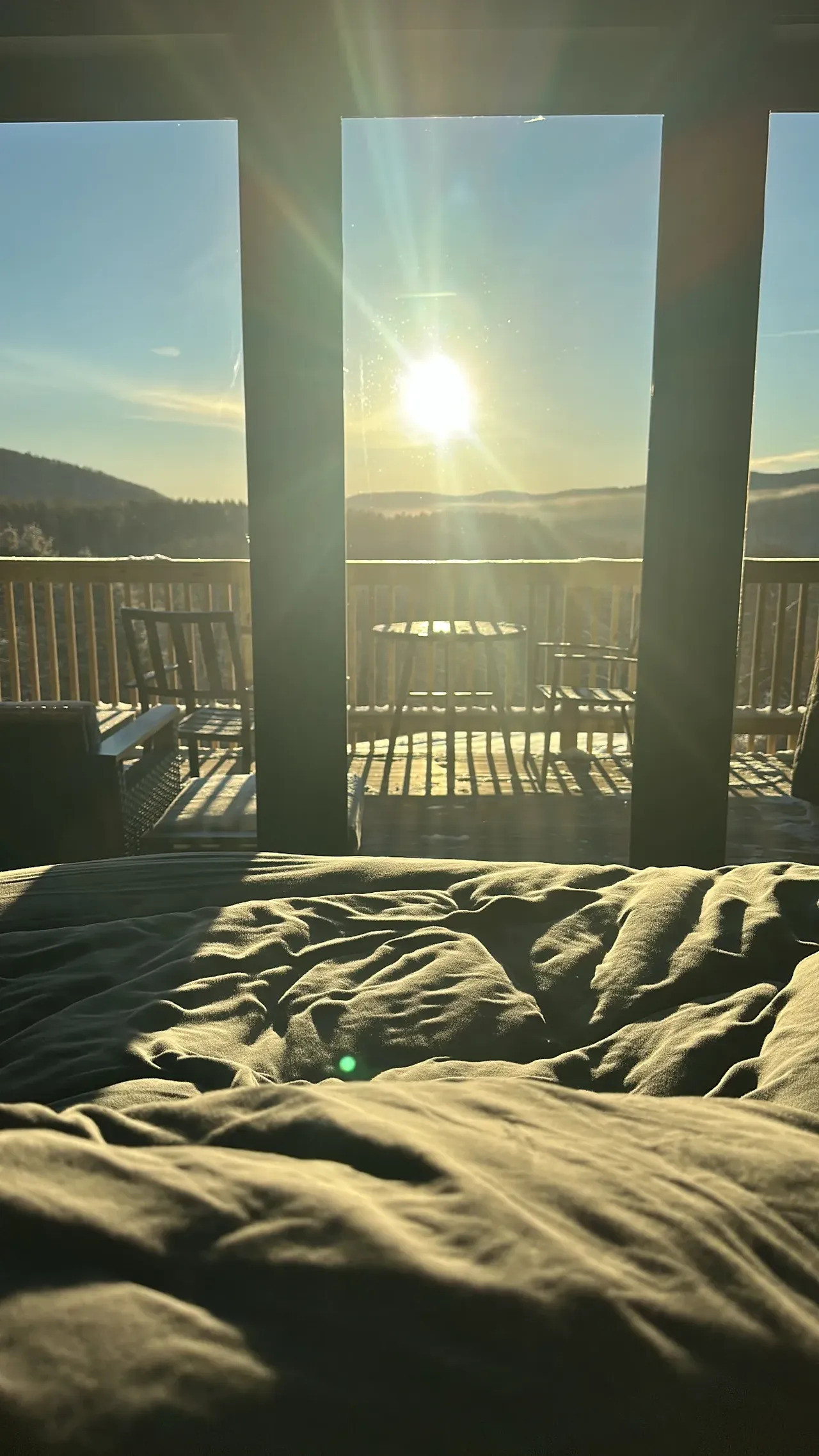 Sunlight streams through cabin windows onto a bed facing a mountain view.