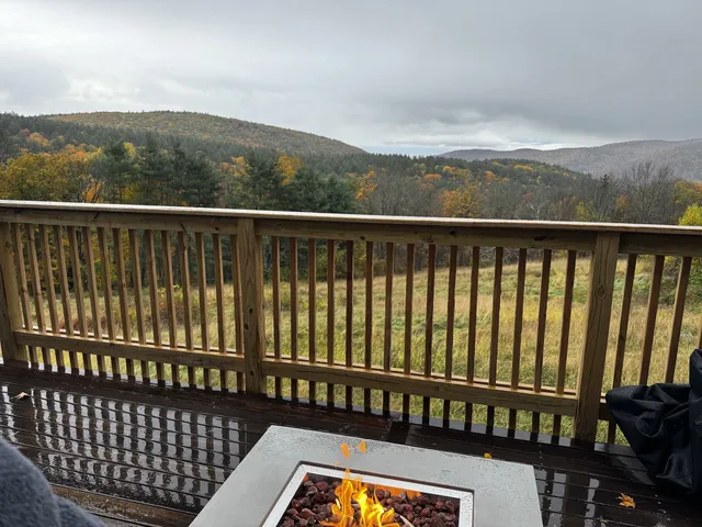 A deck fire pit burns beneath a view of autumn-colored mountain ridges.