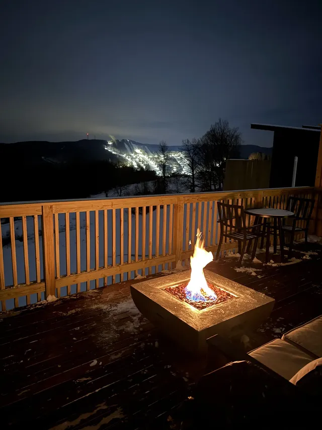 A deck fire pit glows above a snowy mountain valley at night.