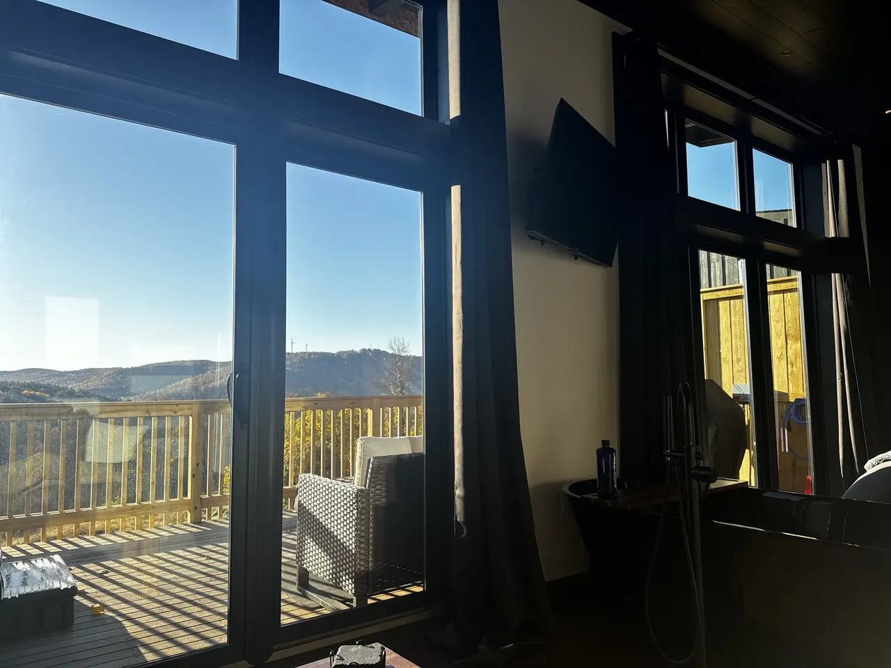 Mountain views show through tall cabin windows beside a deck.